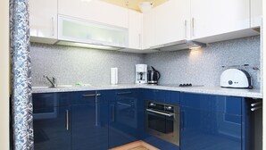 A compact kitchen with white upper cabinets, a blue lower cabinet, a built-in oven, a coffee maker, and a toaster. - Meeresblick - Welcome to the vacation apartment Meeresblick in Kühlungsborn (Kühlungsborn)