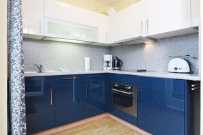 Eine kleine Küche mit weißen Oberschränken, einem blauen Unterschrank, einem eingebauten Backofen, einer Kaffeemaschine und einem Toaster.