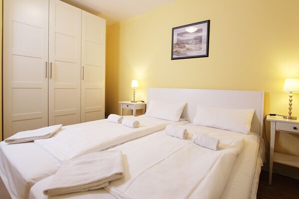 Ein Hotelzimmer mit zwei Betten, weißen Laken, einem Bild an der Wand und Nachttischlampen.