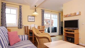 A cozy living room with a sofa, a dining table, wicker chairs, a television, and a view of the outside through large windows. - Meeresblick - Welcome to the vacation apartment Meeresblick in Kühlungsborn (Kühlungsborn)