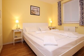 Ein Hotelzimmer mit einem großen Bett, zwei Nachttischen mit Lampen, einem gerahmten Bild an der Wand, einem Fenster mit Vorhängen und einer Heizung.