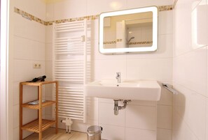 Ein Badezimmer mit einem weißen Waschbecken, einem Spiegel, einem Handtuchhalter und einer kleinen Holztrennwand.