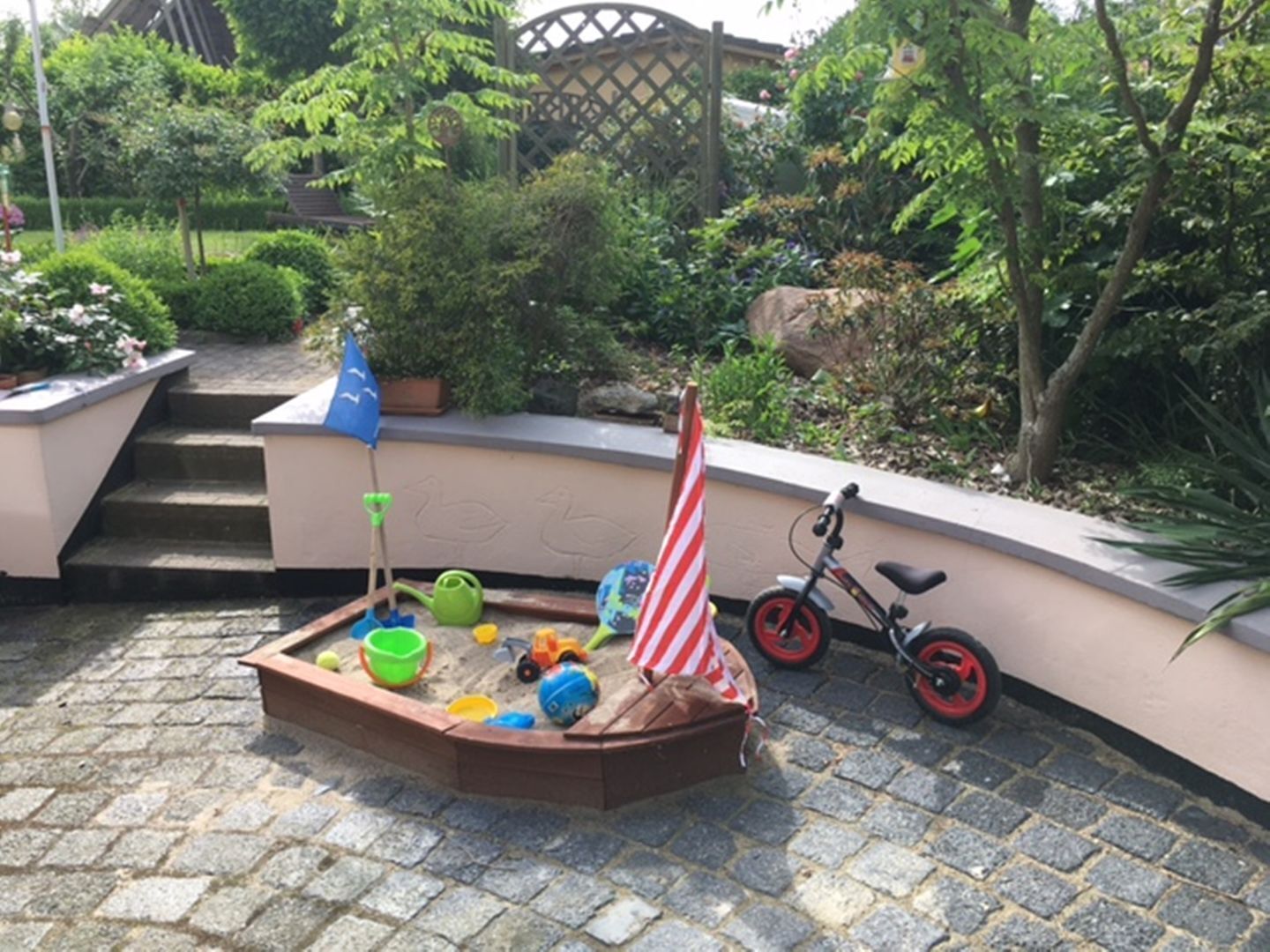 Een speelruimte voor kinderen met een zandbak, speelgoed en een fiets.