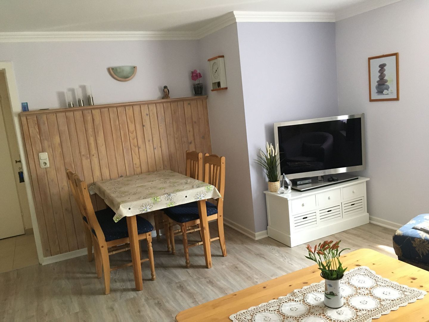 Un coin repas avec une table et des chaises, un téléviseur posé sur un meuble, et une petite plante sur la table.