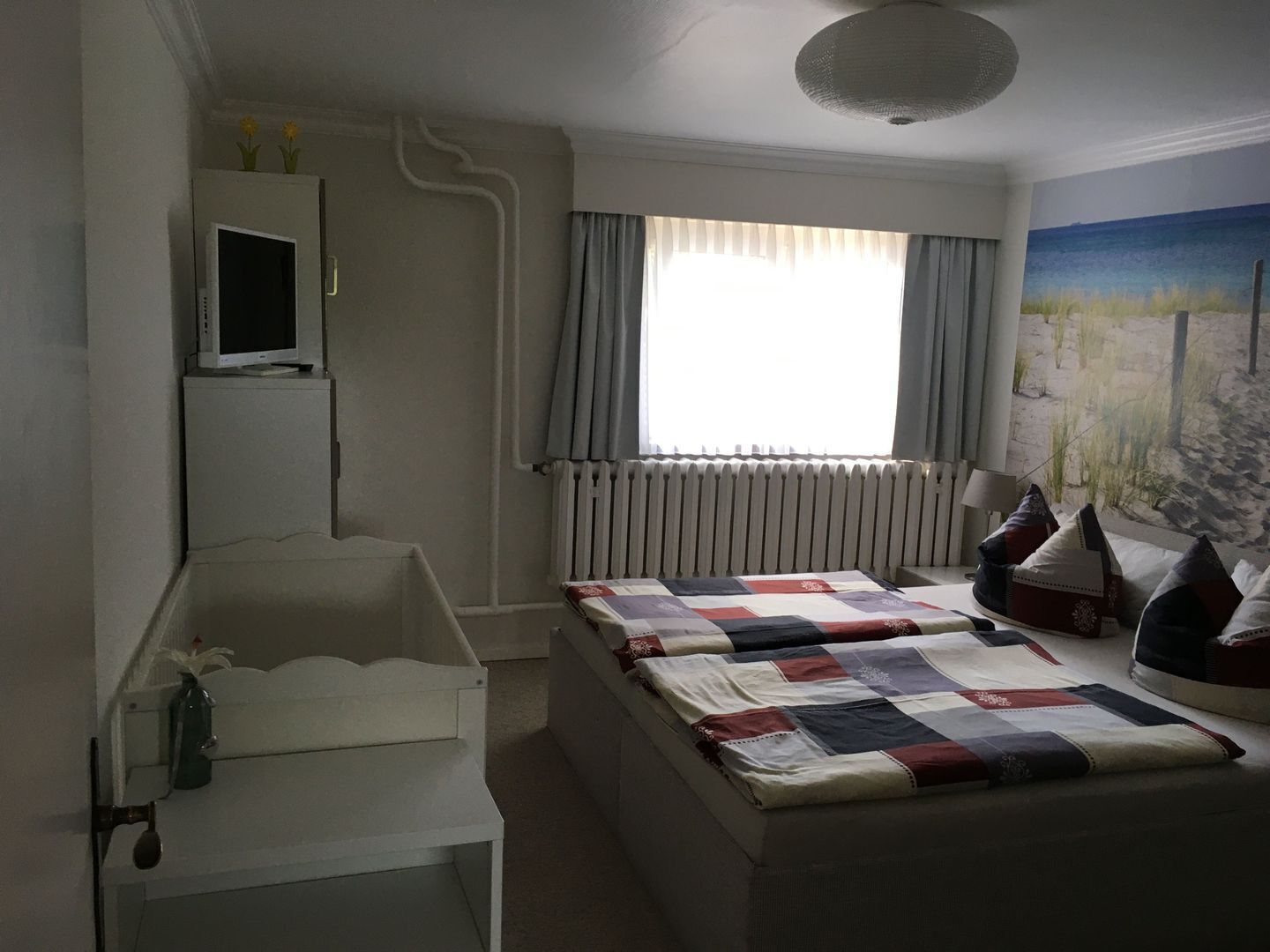 Ein Schlafzimmer mit zwei Betten, einem Fernseher, einem Heizkörper und einem Fenster mit Vorhängen.