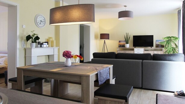 A modern living room with a sofa, a dining table with a vase of flowers, a television, and a lamp.