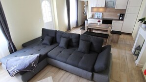 A modern living room with a sectional sofa, a small dining table, and a kitchen area in the background.
