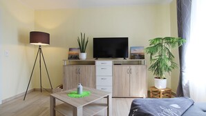 A modern living room with a TV, a dining table, a sofa, and two potted plants.