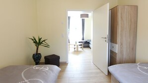 A hotel room with two beds, a wardrobe, a potted plant, and a view into the adjacent room.