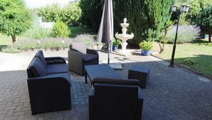 An outdoor patio with wicker furniture, a stone fountain, and a well-maintained garden.