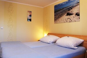 Quarto com cama, duas almofadas, relógio de parede e pintura de uma paisagem praiana.