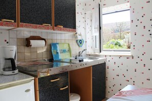 Cozinha compacta com cafeteira, pia e janela com vista para o verde.
