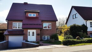 Une maison à deux étages, avec un toit recouvert de tuiles rouges, un garage et un jardin bien entretenu.