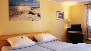 Une chambre d’hôtel avec un lit, deux oreillers, une table de chevet, une lampe et un tableau encadré au mur.
