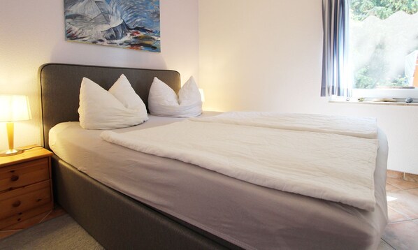 Un lit bien fait, avec du linge de lit blanc et des oreillers, une table de chevet avec une lampe, et un tableau accroché au mur.