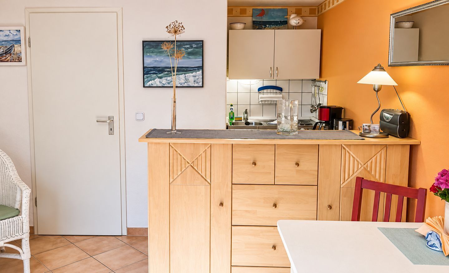 Une cuisine compacte avec un coin repas, une porte blanche et un tableau encadré au mur.