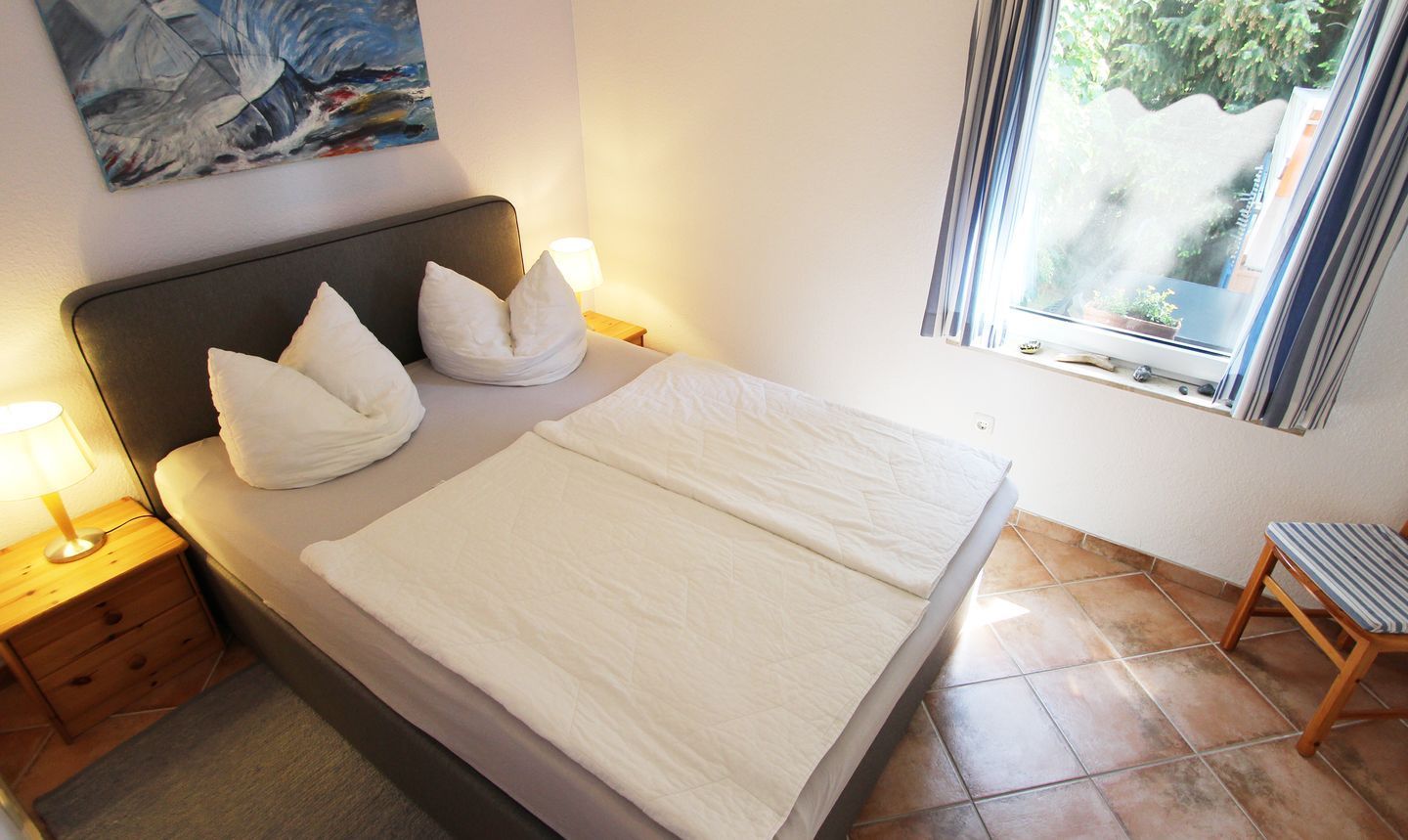 A neatly made bed with pillows, a bedside lamp, and a window with a view of greenery.