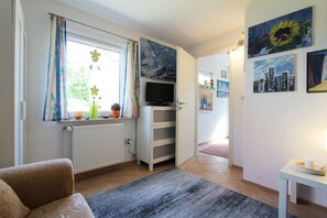 Ein Wohnzimmer mit Fernseher, Heizkörper, Sofa und einem Fenster mit Vorhängen.
