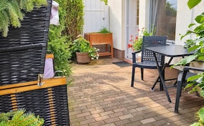 Un patio con una mesa y sillas, una jardinera de madera y suelo de ladrillo.