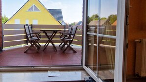 A balcony with a table and chairs, a yellow house in the background, and a clear sky. - Am Obstgarten - Comfortable vacation apartment with covered balcony near the beach in (Kühlungsborn)