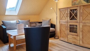 A cozy loft bedroom with a sloped ceiling, a wooden cabinet with glass doors, a black armchair, a small wooden table, and a skylight. - Am Obstgarten - Comfortable vacation apartment with covered balcony near the beach in (Kühlungsborn)