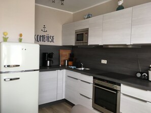 A modern kitchen with white cabinets, a built-in microwave, a coffee maker, and a kettle.