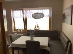 A dining area with a table, chairs, a bench, and a window with curtains.