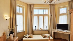 Ein Hotelzimmer mit Bett, Schreibtisch mit Fernseher, Fenster mit Vorhängen und einer Lampe.