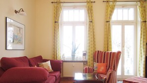 Ein Wohnzimmer mit einem roten Sofa, einem gestreiften Sessel, einem Glastisch und gelben Vorhängen.