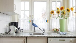 Eine Küche mit Spüle, Kaffeemaschine, Vogel-Skulptur und Blumen in einer Vase.