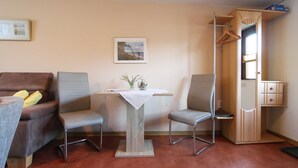 Una habitación con un sofá, dos sillones, una mesita con un jarrón, un armario y una ventana.