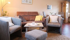 Una sala de estar con un sofá marrón, dos sillones grises, una mesa de centro y una lámpara.