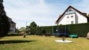 Ett bostadsområde med en välskött gräsmatta, en studsmatta och en häck.