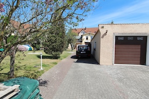 A narrow driveway leading to a garage with a parked car. There is a tent and a tree in the foreground.