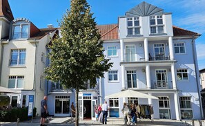 Ein mehrstöckiges Gebäude mit einem zentralen Eingang, großen Fenstern und Balkonen.
