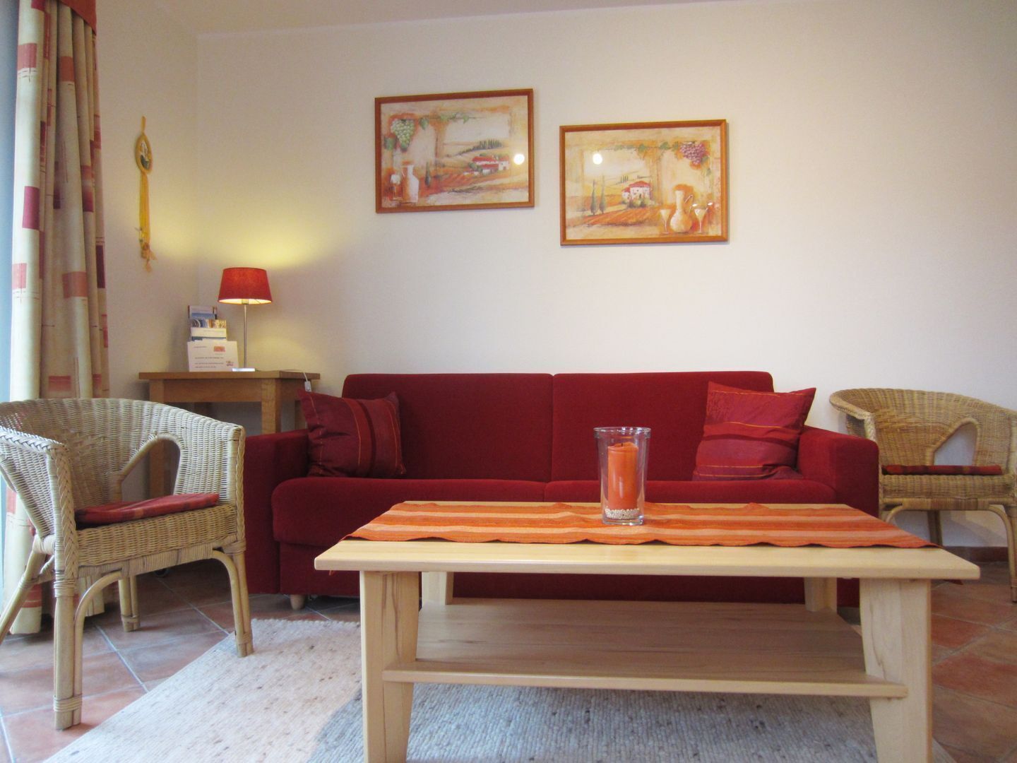 Una sala de estar con un sofá rojo, dos sillas de mimbre, una mesa de centro de madera y dos cuadros enmarcados en la pared.
