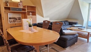 Un soggiorno moderno con un tavolo rotondo in legno, un divano grigio scuro e un tavolino. Si vede una libreria con diversi oggetti e un quadro appeso al muro.