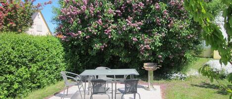 A patio with a table and chairs, surrounded by lush greenery and flowering bushes.