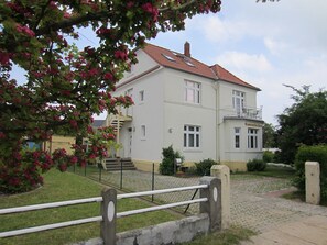 Un edificio a due piani con tetto in tegole rosse, un balcone al secondo piano e un piccolo giardino recintato.