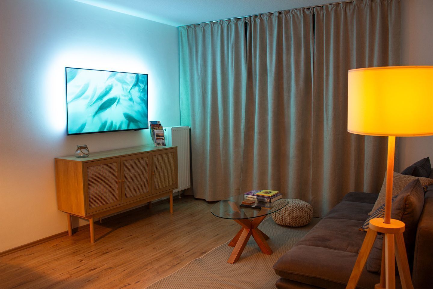 Un salon équipé d’un téléviseur à écran plat, d’un canapé, d’une lampe, d’une table basse en verre et d’un radiateur.