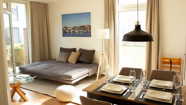 A bedroom with a bed, bedside table, lamp, and a dining area with a table set for two.