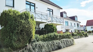 A modern residential building with a balcony, a paved driveway, and well-maintained hedges.
