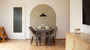A dining area with a table set for two, a wooden floor, a door with frosted glass, and a hanging pendant light.