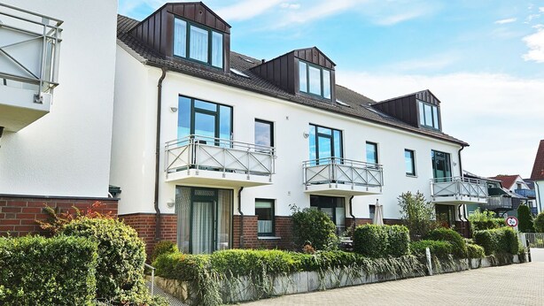 A row of modern townhouses with balconies, brick facades, and a paved driveway.