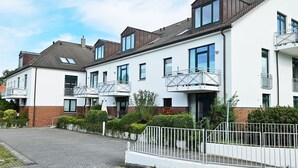 A row of modern townhouses with balconies, a paved driveway, and a white fence.