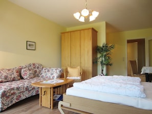Um quarto aconchegante com uma cama, um sofá, um armário de madeira, uma mesa e um vaso de planta.
