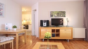 A modern living room with a wooden dining table, a glass coffee table, a TV, speakers, and a radiator.