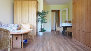 A room with a wooden wardrobe, a dining table with chairs, a wicker sofa, and a potted plant.