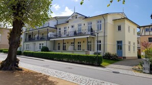 A two-story building with a balcony, a tree in front, and a cobblestone pathway.