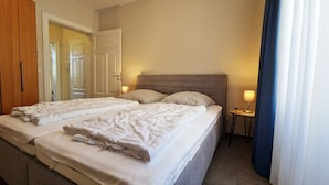 A double bed with two pillows, a bedside table with a lamp, and a door in the background.